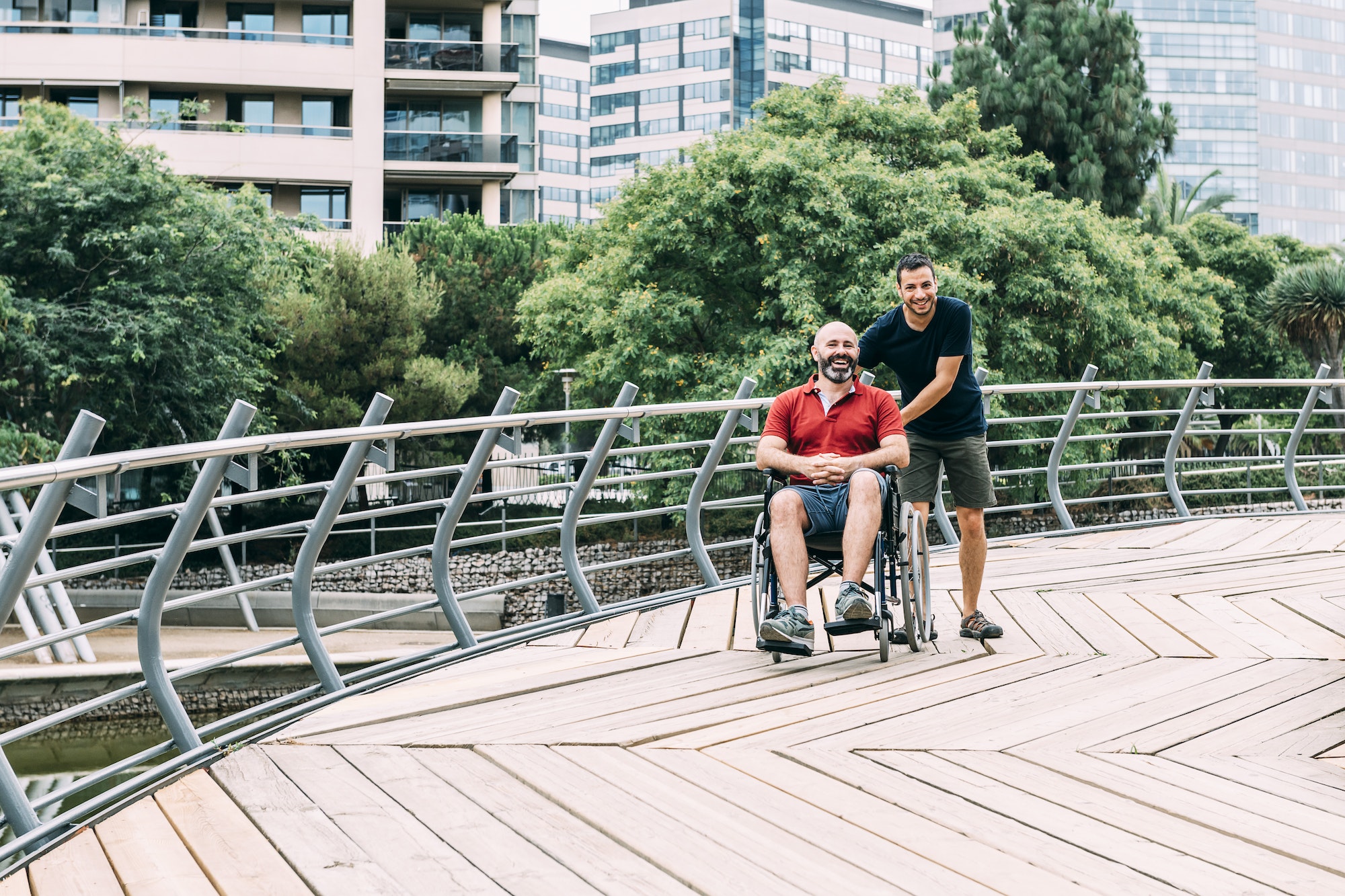 man in wheelchair walking at park with a friend