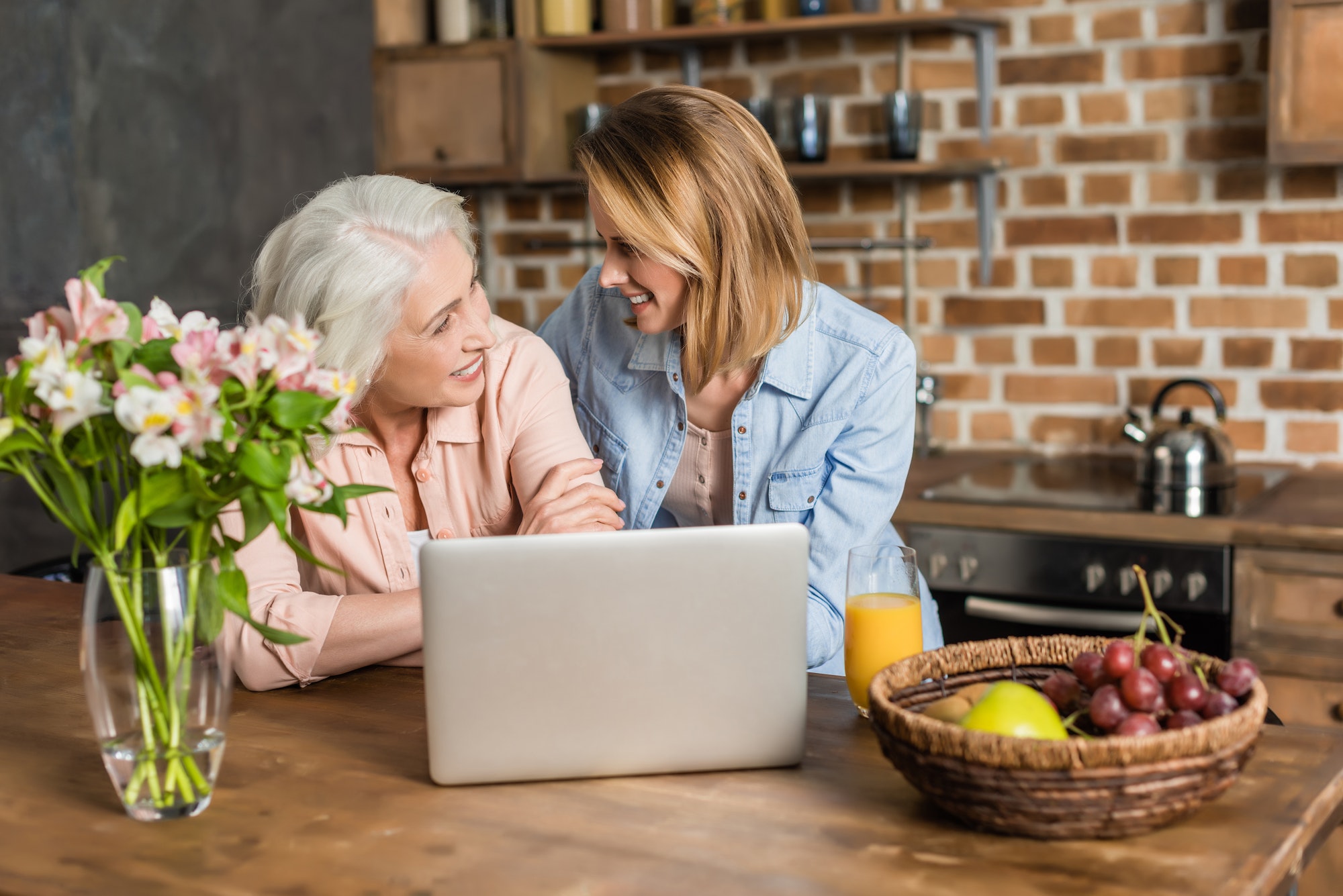 two women, senior and young using laptop at table in kitchen